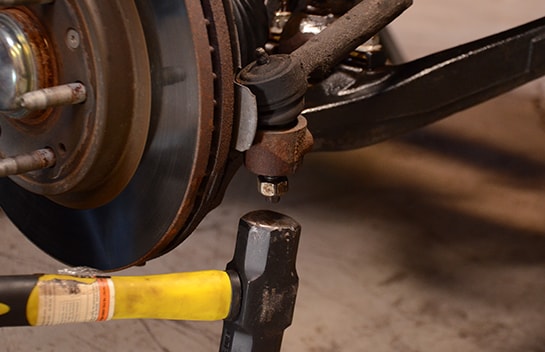 Mechanic using a sledgehammer to loosen the tie rod stud from the housing